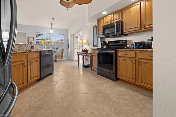 Kitchen with lofted ceiling, dark stone counters, black appliances, light tile patterned floors, and decorative light fixtures