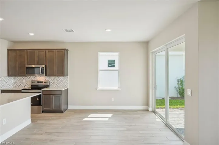 Kitchen featuring light hardwood / wood-style flooring, dark brown cabinets, appliances with stainless steel finishes, and tasteful backsplash