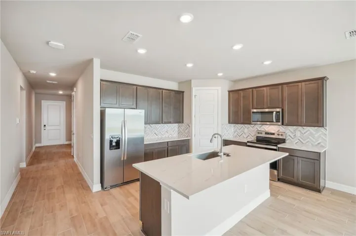 Kitchen featuring light stone counters, a kitchen island with sink, sink, light hardwood / wood-style flooring, and appliances with stainless steel finishes