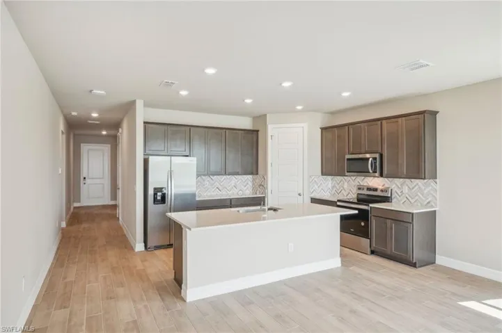 Kitchen featuring light wood-type flooring, a kitchen island with sink, sink, decorative backsplash, and appliances with stainless steel finishes