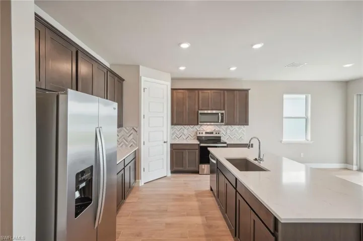 Kitchen featuring dark brown cabinetry, sink, light hardwood / wood-style flooring, stainless steel appliances, and light stone countertops