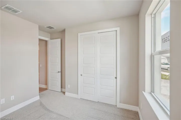 Unfurnished bedroom featuring a closet, multiple windows, and light colored carpet