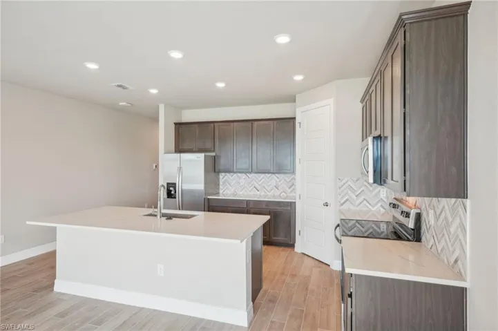 Kitchen featuring appliances with stainless steel finishes, a kitchen island with sink, sink, and light hardwood / wood-style flooring
