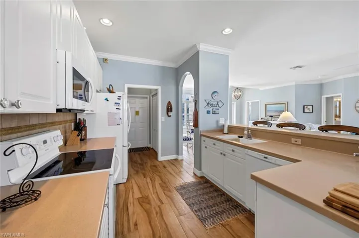 Kitchen with sink, white cabinets, ornamental molding, light hardwood / wood-style floors, and white appliances