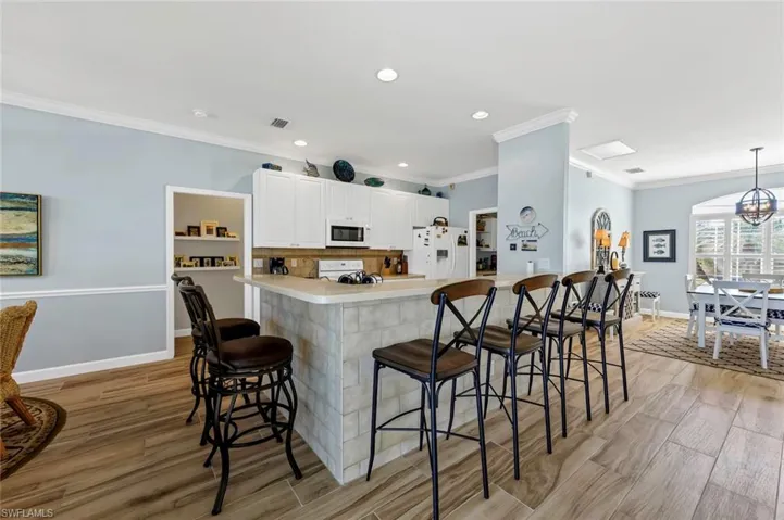 Kitchen featuring pendant lighting, white cabinetry, a kitchen breakfast bar, white appliances, and light hardwood / wood-style flooring