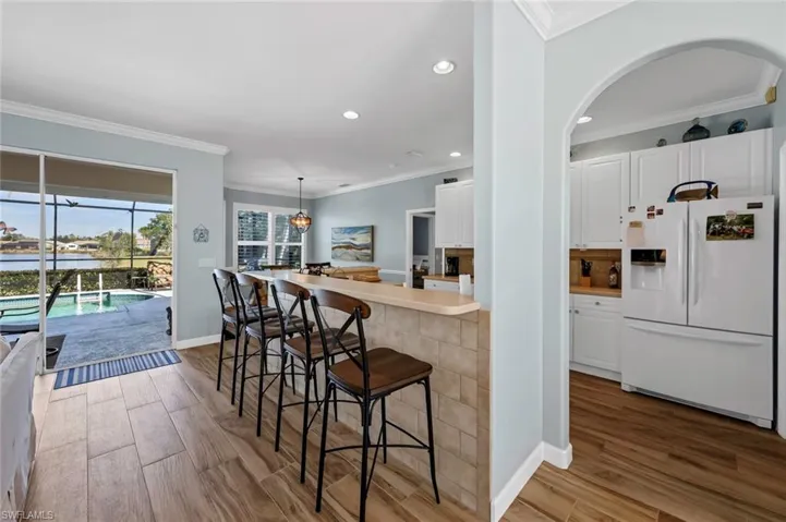 Kitchen with hardwood / wood-style flooring, white refrigerator with ice dispenser, white cabinets, and a kitchen breakfast bar
