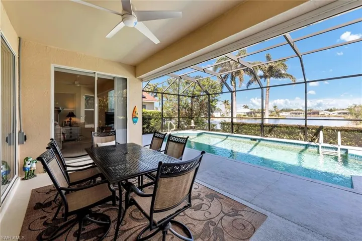 View of swimming pool with a water view, ceiling fan, glass enclosure, and a patio