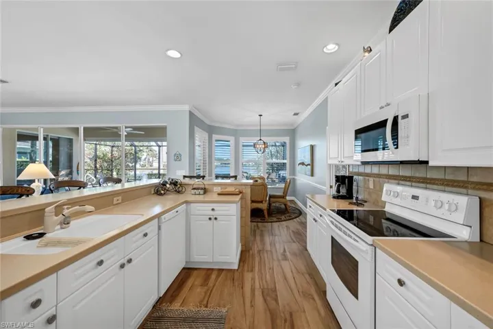 Kitchen with sink, white appliances, ornamental molding, white cabinets, and decorative light fixtures