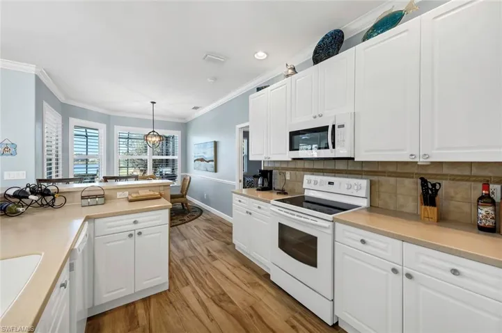 Kitchen featuring white cabinetry, crown molding, light hardwood / wood-style flooring, pendant lighting, and white appliances