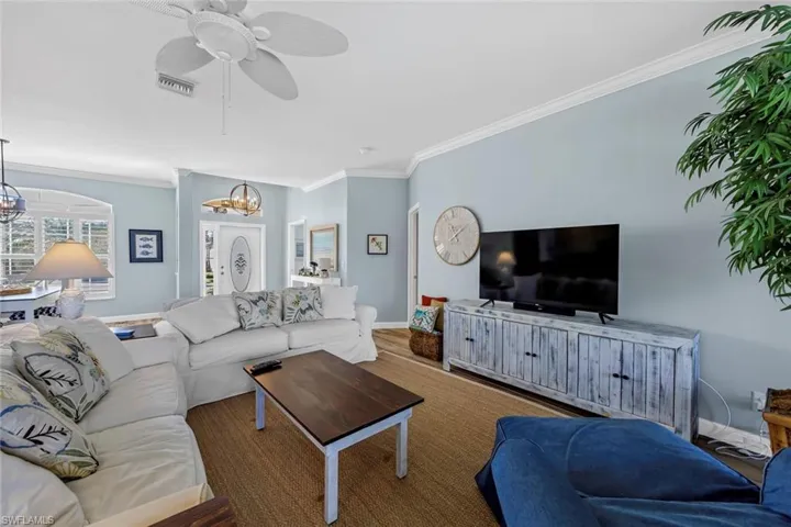 Living room with crown molding, wood-type flooring, and ceiling fan with notable chandelier