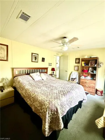Bedroom featuring a wooden headboard, light yellow walls, and a ceiling fan with integrated lighting