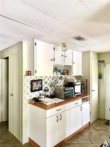Kitchenette featuring white cabinetry with black hardware, wood-finish countertops, a decorative lattice backsplash, and tiled flooring