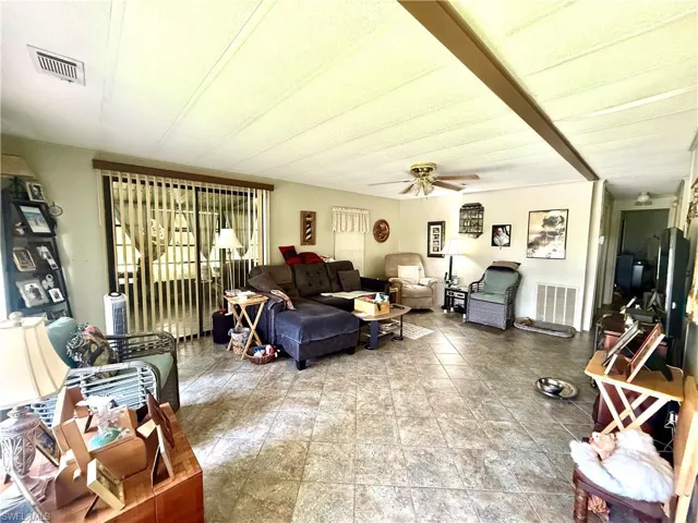 Spacious living area featuring tile flooring, ceiling fan, and sliding glass doors with vertical blinds