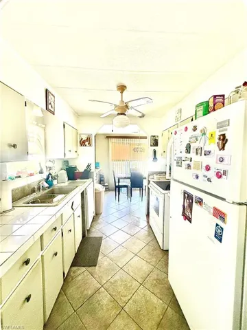 Galley-style kitchen featuring tiled flooring, white cabinetry, and a ceiling fan with integrated lighting