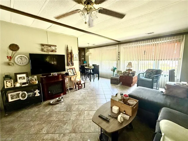 Spacious living area featuring tile flooring, a textured ceiling with exposed beams, and a ceiling fan