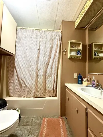Bathroom featuring a white bathtub with a shower curtain rod, a white toilet, and a vanity with an integrated sink and base cabinetry