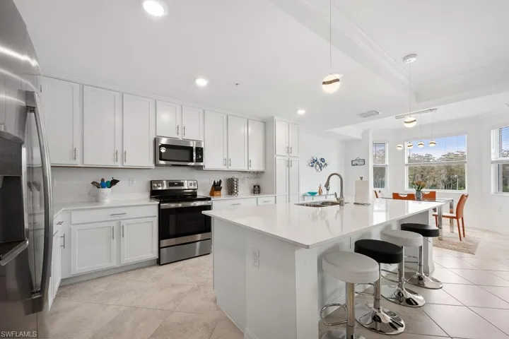 Kitchen with pendant lighting, stainless steel appliances, an island with sink, white cabinetry, and a breakfast bar