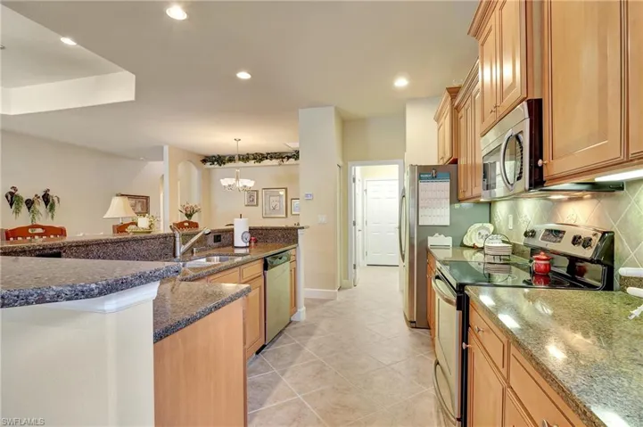 Kitchen with dark stone countertops, light tile patterned floors, backsplash, appliances with stainless steel finishes, and pendant lighting