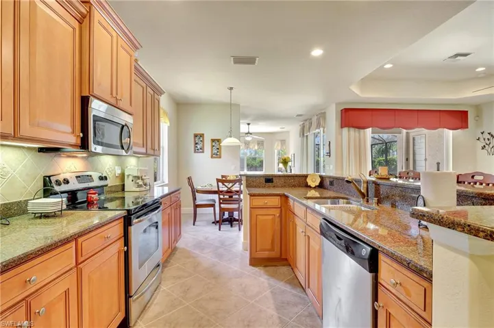 Kitchen with stainless steel appliances, sink, light stone countertops, light tile patterned floors, and backsplash