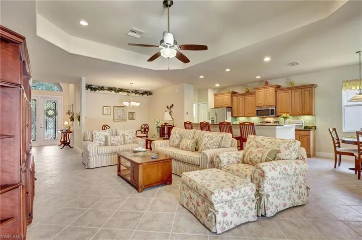 Living room featuring ceiling fan with notable chandelier, light tile patterned floors, and a tray ceiling