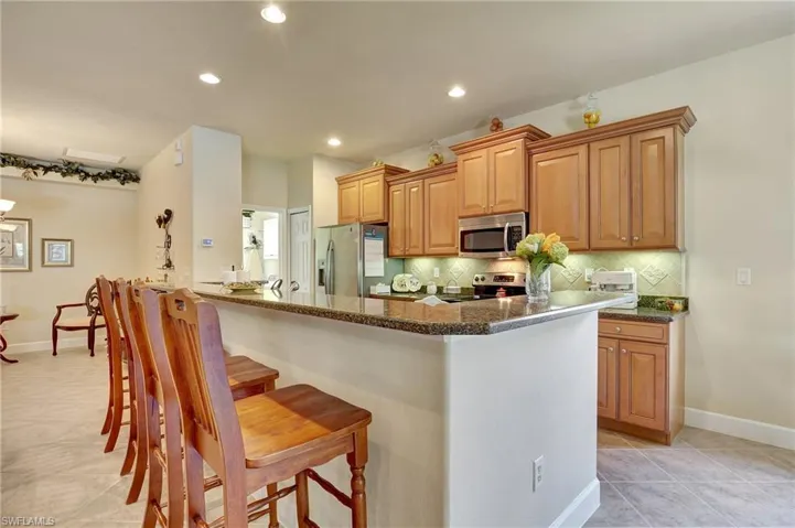 Kitchen with appliances with stainless steel finishes, dark stone counters, tasteful backsplash, a breakfast bar, and light tile patterned floors