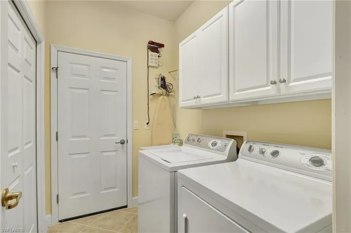 Clothes washing area with cabinets, washer and clothes dryer, and light tile patterned floors