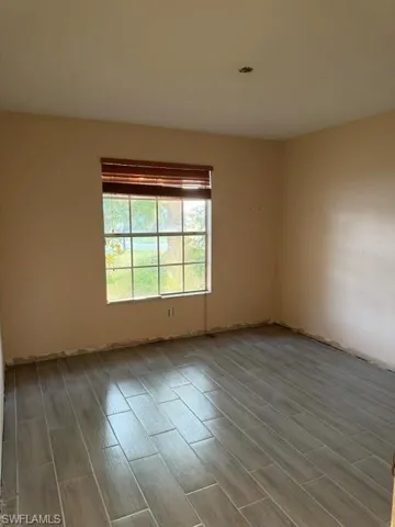 Room featuring wood-finish tile flooring, a window with horizontal blinds, and a neutral wall color