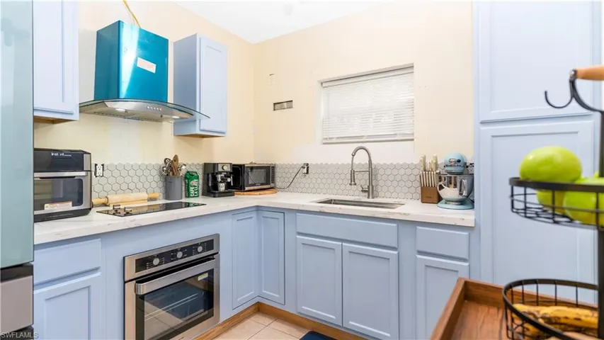 Kitchen featuring light stone countertops, wall chimney exhaust hood, sink, appliances with stainless steel finishes, and backsplash