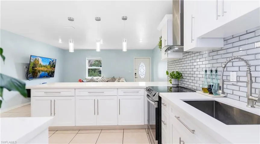 Kitchen with tasteful backsplash, white cabinets, sink, decorative light fixtures, and electric range