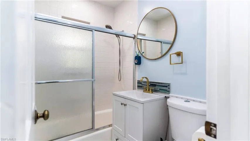 Full bathroom with enclosed tub / shower combo, vanity, and toilet