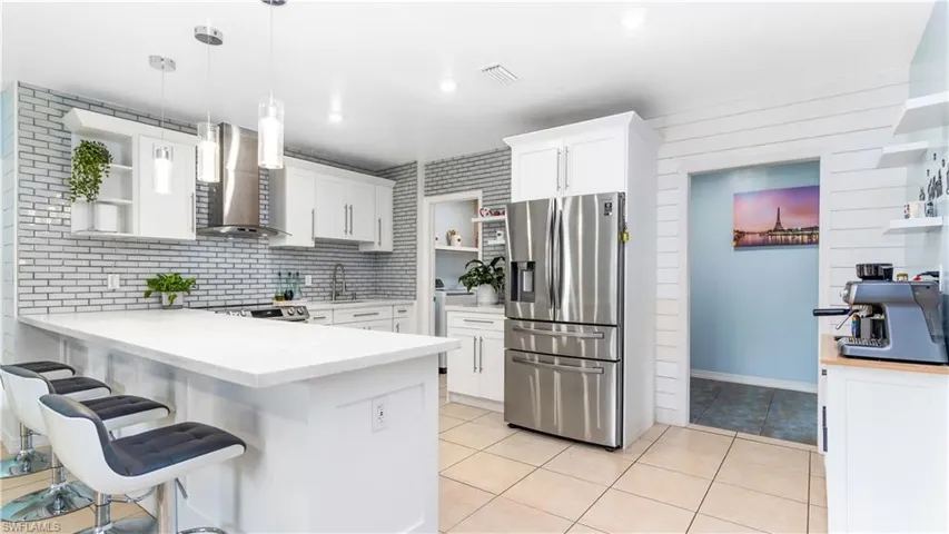 Kitchen with pendant lighting, kitchen peninsula, wall chimney exhaust hood, white cabinetry, and stainless steel appliances