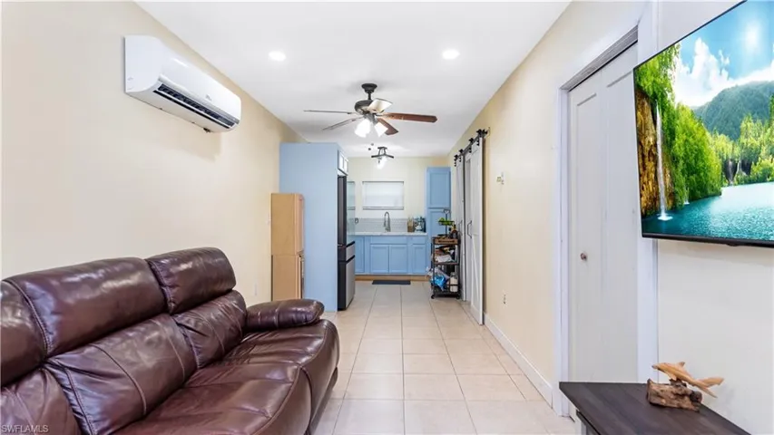 Living room with a barn door, a wall unit AC, ceiling fan, sink, and light tile patterned floors