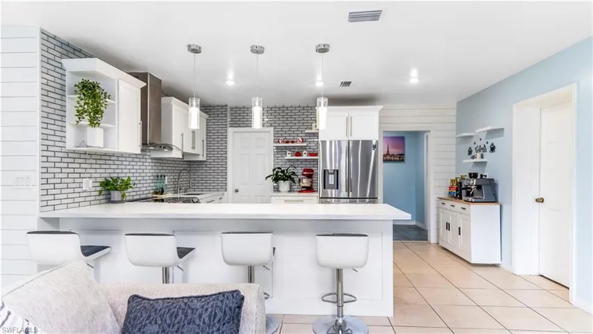 Kitchen with white cabinets, kitchen peninsula, pendant lighting, stainless steel fridge with ice dispenser, and a kitchen bar
