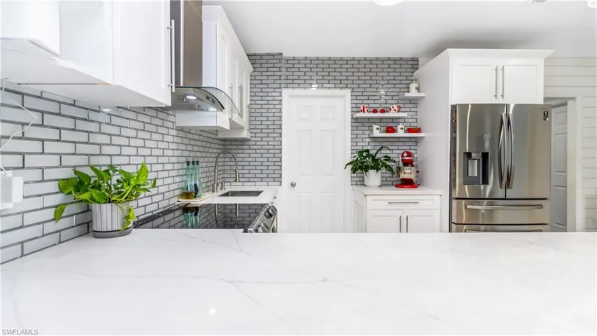 Kitchen featuring light stone counters, wall chimney exhaust hood, sink, white cabinetry, and stainless steel fridge with ice dispenser