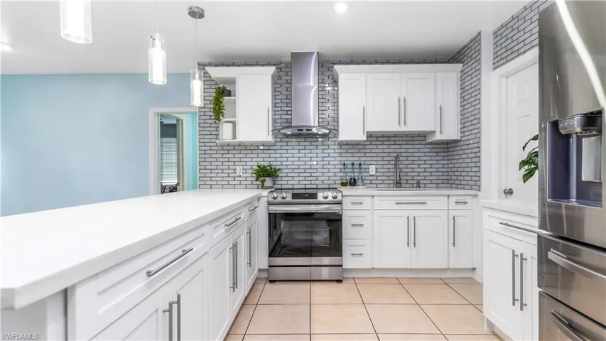 Kitchen with white cabinets, sink, wall chimney range hood, hanging light fixtures, and appliances with stainless steel finishes