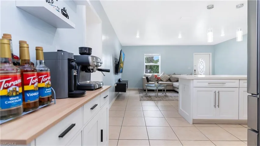 Kitchen featuring pendant lighting, light tile patterned flooring, kitchen peninsula, butcher block countertops, and white cabinetry