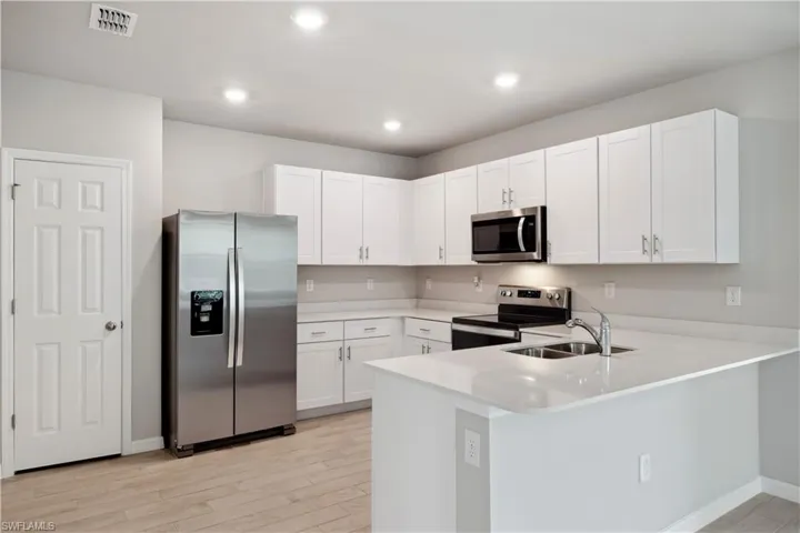 Kitchen featuring white cabinetry, light hardwood / wood-style floors, stainless steel appliances, kitchen peninsula, and sink