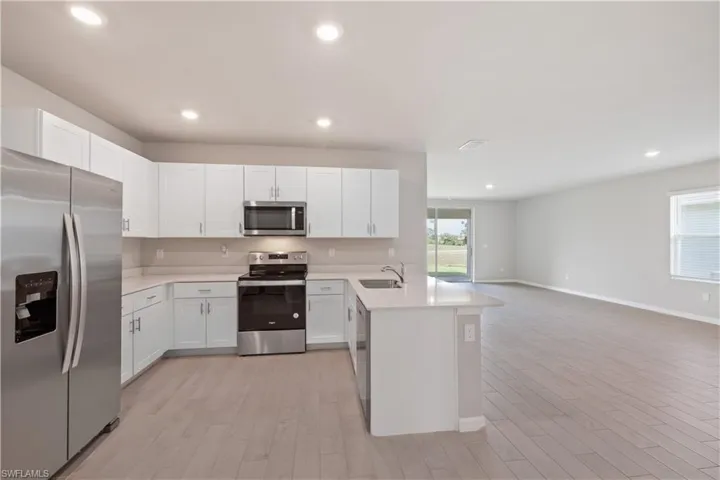 Kitchen featuring light wood-type flooring, stainless steel appliances, white cabinets, kitchen peninsula, and sink