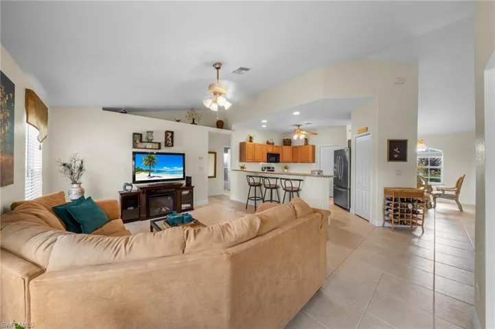 Living room featuring ceiling fan, light tile patterned flooring, vaulted ceiling, and baseboards