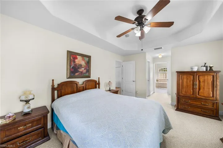 Bedroom with a raised ceiling, light carpet, baseboards, connected bathroom, and ceiling fan