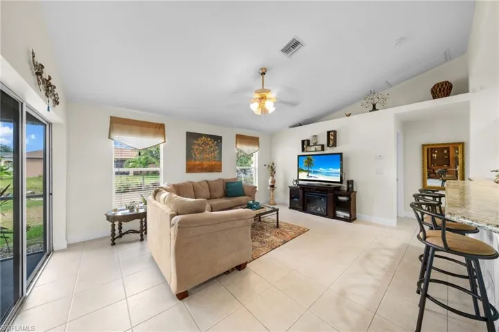 Living room with vaulted ceiling, light tile patterned floors, ceiling fan, and baseboards