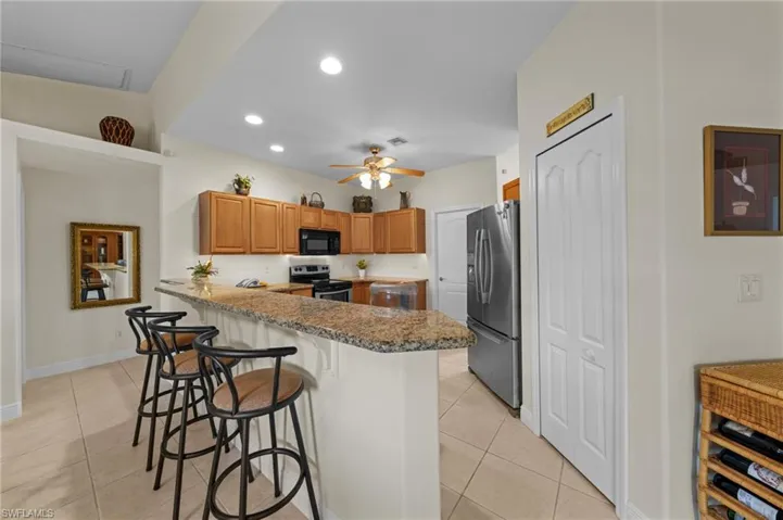Kitchen with stainless steel appliances, light tile patterned floors, a peninsula, a kitchen breakfast bar, and ceiling fan