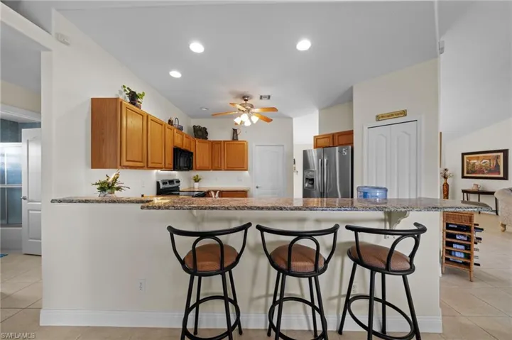 Kitchen featuring appliances with stainless steel finishes, light tile patterned floors, a peninsula, ceiling fan, and a breakfast bar area