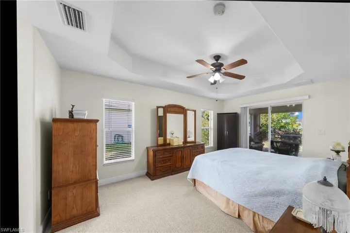 Bedroom featuring a tray ceiling, access to exterior, light carpet, baseboards, and a ceiling fan