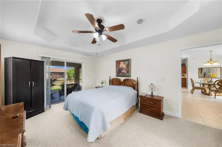 Bedroom with a raised ceiling, access to outside, light carpet, baseboards, and a ceiling fan