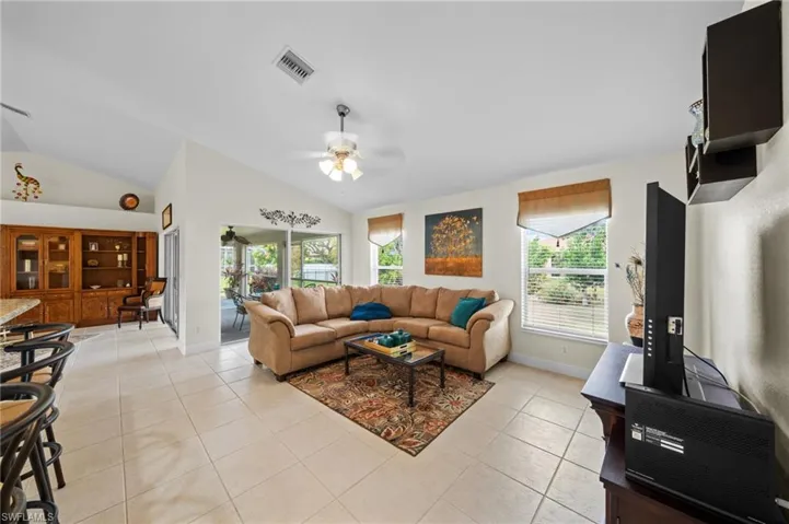 Living area featuring lofted ceiling, ceiling fan, light tile patterned flooring, and baseboards