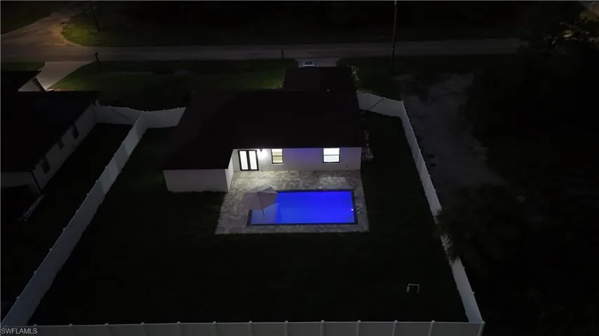 Rectangular inground pool with paver patio, enclosed by a white vinyl privacy fence and manicured lawn