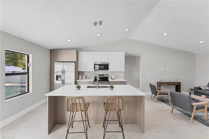 Kitchen featuring white upper cabinetry, wood-finish lower cabinetry, a central island with a solid-surface countertop, integrated stainless steel appliances, and recessed lighting under a vaulted ceiling