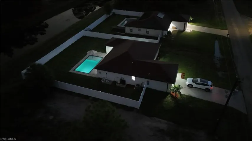 Aerial perspective of a property featuring an in-ground swimming pool, a perimeter vinyl privacy fence, a multi-pitched roofline, and a concrete driveway