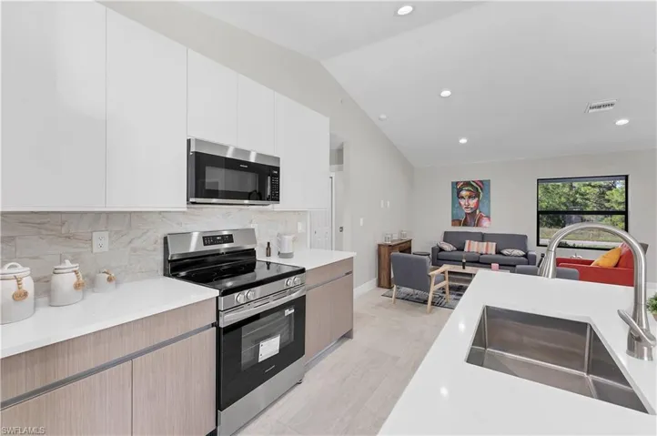 Kitchen featuring slab-style cabinetry, solid-surface countertops, stone-patterned backsplash, stainless steel appliances, and a vaulted ceiling